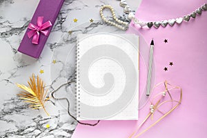 Set of women`s accessories desk - notebook with pen, gifts, jewelry, bracelet, golden palm leaf on pink marble background.