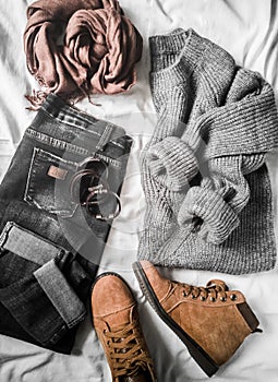 Set of women`s autumn, winter clothes on a light background - jeans, gray pullover oversize, suede brown boots and scarf. Fashion