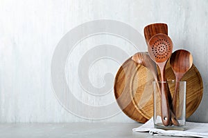 Set of wooden kitchen utensils and plates on light grey table. Space for text