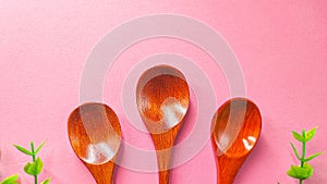 Set of wooden spoon three-piece and green plastic leaf isolated on pink background. Concept: kitchen utensils made from natural