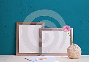 Set for writing, pink gerbera flower in an old vase, two gray frames for a photo on a blue background