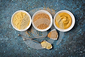 Set of yellow mustard sauce, powder and seeds in small bowls with silver spoons
