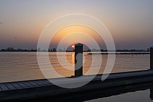 The setting sun almost disappears behind one of the bollards of a landing stage at Lake Zoetermeerse Plas in Zoetermeer, The Nethe