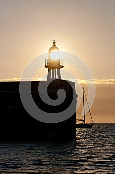 The setting sun shines through a lighthouse on a Port Erin Harbour