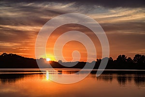 Setting sun over silhouettes of trees with reflection in lake