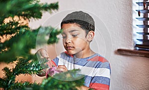 Setting up for Christmas. a carefree little boy putting up Christmas decorations on a tree at home during Christmas time