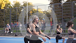 Seven athletic lean girls in sportswear doing squat exercises during fitness workout in the park