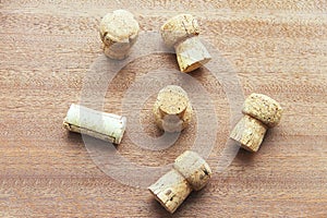 Seven caps of cork champagne randomly scattered on a wooden board