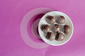 Seven chocolates in a white porcelain saucer on a pink background