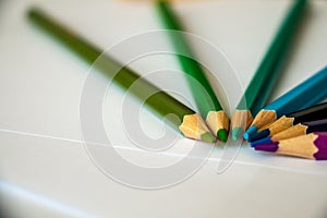 Seven colored pencils lie in a semicircle on white sheets of paper
