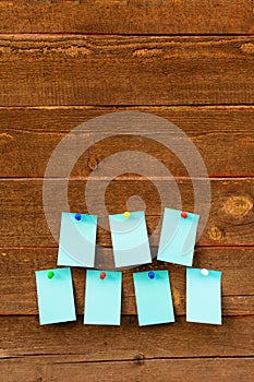 Seven empty blue paper with colorful pins over wooden background