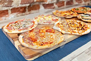 Seven pizzas on a wooden board, fresh out of the oven with focus on pepperoni pizza