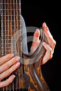 Seven-string electric guitar made of dark wood and human hands, shot on a dark background. Background for musical instruments and