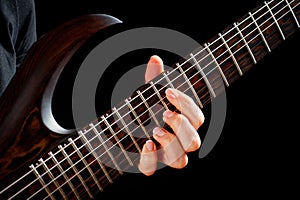 Seven-string electric guitar made of dark wood and human hands, shot on a dark background. Background for musical instruments and