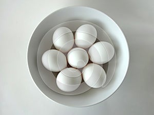 Seven White Eggs in a Round White Bowl against a White Background