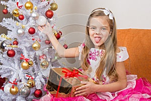 Seven-year girl in beautiful dress sits with a gift and showed language to frame photo