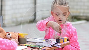 Seven-year girl hard dunks brush in a jar with watercolor paint drawing on the album, sitting at table with another girl