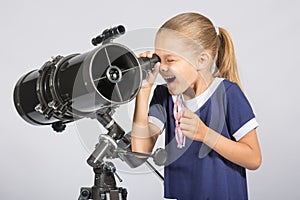 Seven-year girl with interest and mouth open looking into the reflector telescope and looks at the sky