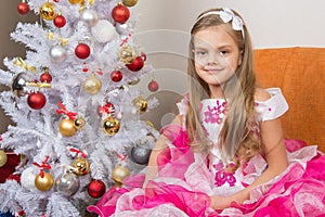 Seven-year girl sitting on a sofa in beautiful dress the Christmas tree