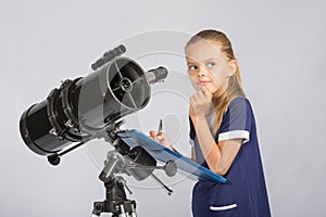 Seven-year girl thoughtful looking at the sky, making the recording of observations in the telescope