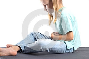 A seven-year-old blonde caucasian girl sits and holds her stomach. The concept of abdominal pain in children due to poor