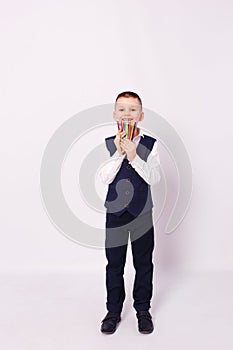 Seven-year-old boy in school uniform holds colored pencils on white background