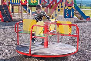 Seven-year-old boy spinning on the carousel on the Playground.
