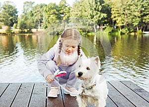 A seven-year-old girl with a small white dog stands on a bridge near the lake and looks at the water.