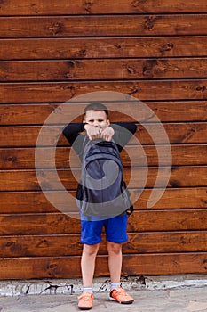 Seven-year-old schoolboy in sportswear holds a heavy backpack