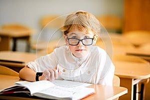 Seven years old child with glasses writing his homework at school. Boy studing at table on class background