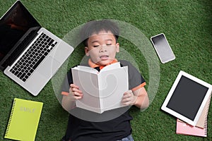 Seven years old child reading a book lying on the grass