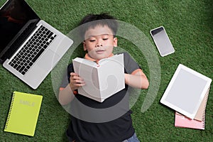 Seven years old child reading a book lying on the grass