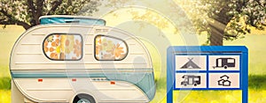 Seventies caravan with camp site greeting sign in front of blooming trees with summer sunlight