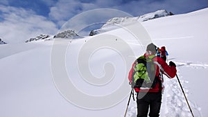 Several backcountry skiers hike and climb to a remote mountain peak in Switzerland on a beautiful winter day