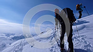 Several backcountry skiers hike and climb to a remote mountain peak in Switzerland on a beautiful winter day