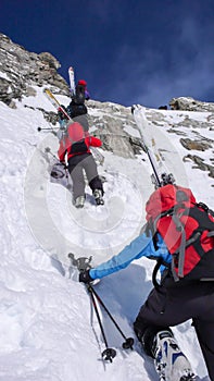 Several backcountry skiers hike and climb to a remote mountain peak in Switzerland on a beautiful winter day