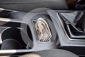 Several banknotes American dollars lie in the niche of the central console of the car. The money in the car