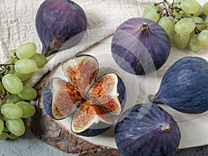 Several berries of figs and small bunches of grapes lie on a table on a circle of natural sawn wood and a linen napkin.