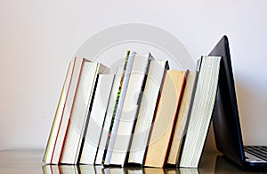 Several books resting on a laptop, as if it were a bookend