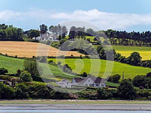 Several buildings and trees on a hill. Irish summer landscape. Picturesque countryside. Farm fields under a blue sky, house on