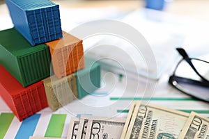 Several colorful cargo containers with us dollar bills and glasses on financial reports.