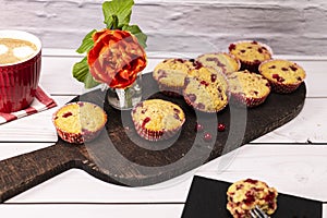 Several currant muffin served on a rustic board with a cup of cappuccino