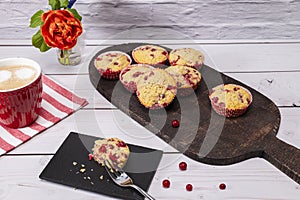 Several currant muffin served on a rustic board with a cup of cappuccino