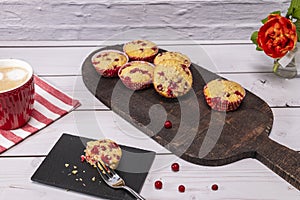 Several currant muffin served on a rustic board with a cup of cappuccino