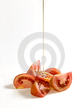 Several cuts of red tomato with a jet of oil falling on them photo