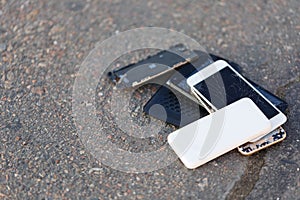 Several broken smartphones are on the asphalt.