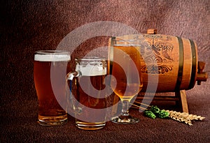 Several different glasses with light beer, a wooden keg, ears of wheat and hops on a brown abstract background