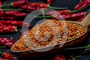 Several dried chilli peppers and crushed peppers on an old s