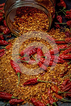 Several dried chilli peppers and crushed peppers on an old s