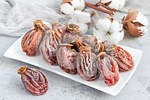 Several dried persimmon on white plate, gray background, horizontal